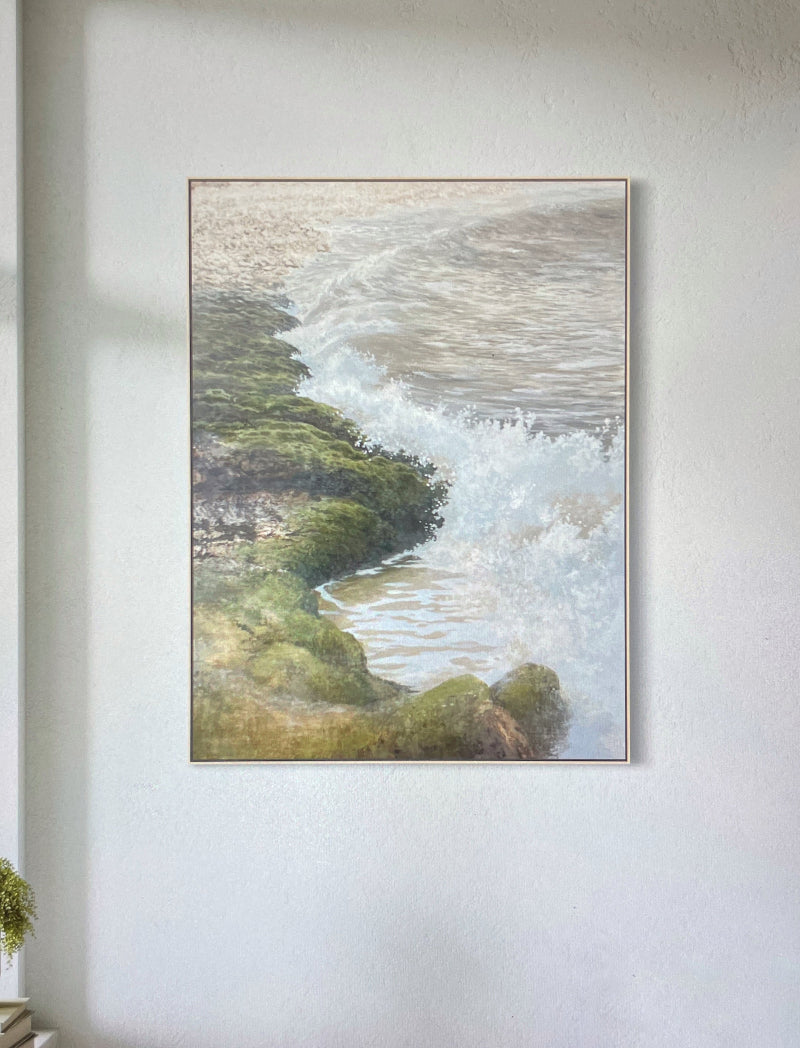 Framed artwork by Desmond Sweeney of a coastal scene with waves and greenery on a white wall.
