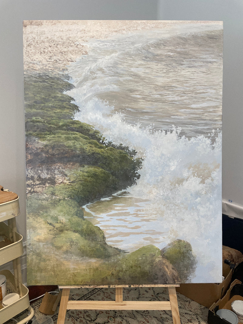 seascape artwork by Desmond Sweeney of a coastal scene with waves and greenery on an easel.